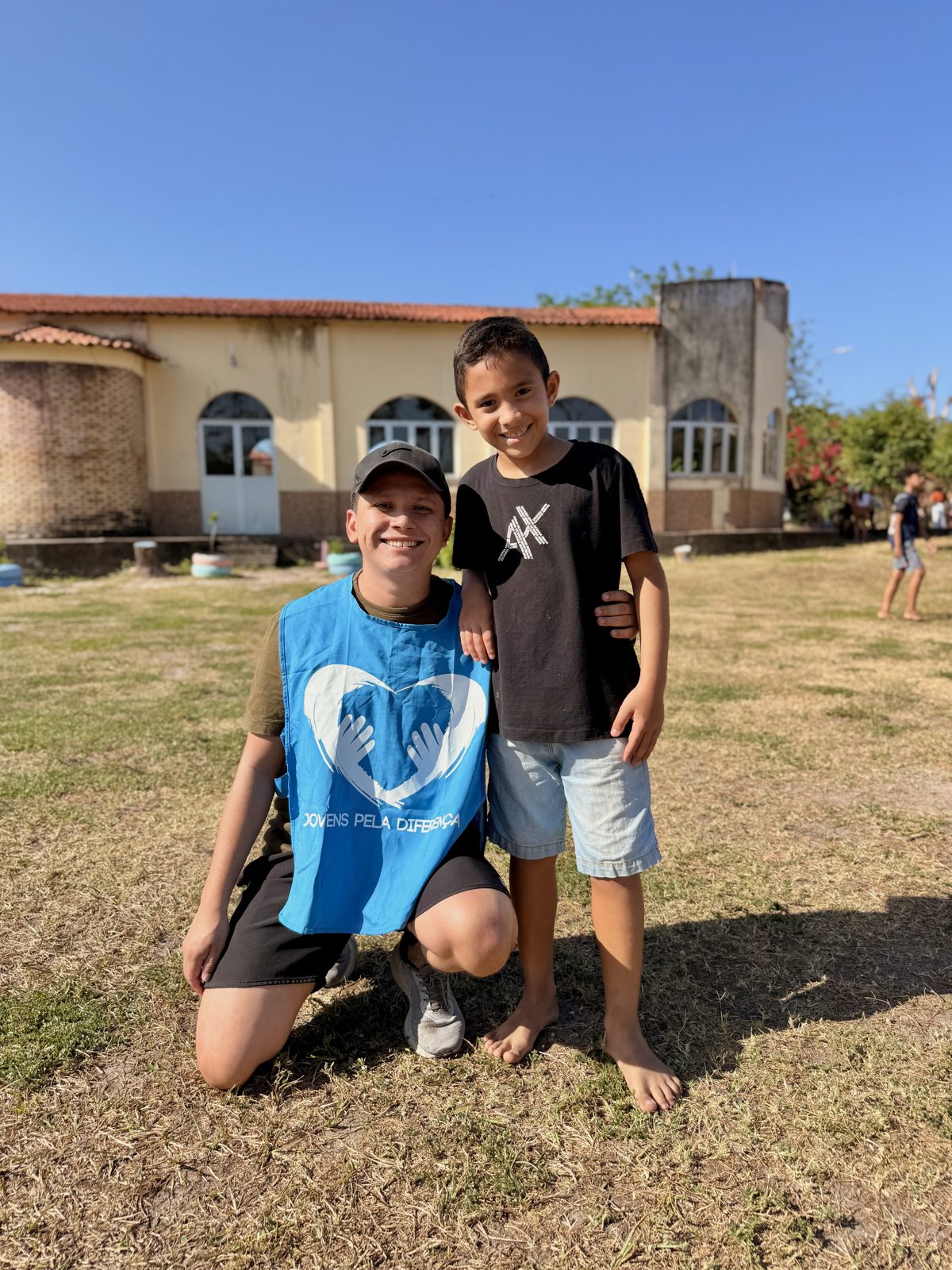 Voluntário agachado ao lado de um menino em um campo aberto.